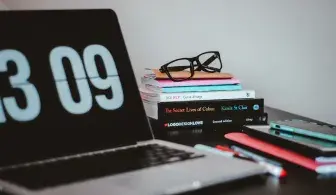 На столе стоит ноутбук, книги, очки и смартфон